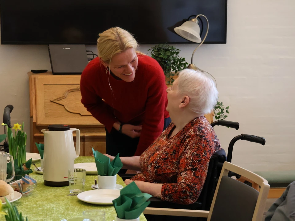 Mette Kierkgaard hilser på ældre dame ved kaffebord